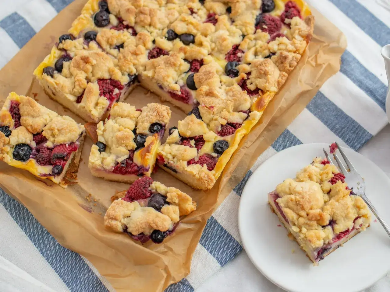 Pyszne przepisy z kruchego ciasta: jagody i maliny pod kruszonką na prostokątnej blasze. Jeden kawałek na talerzyku.