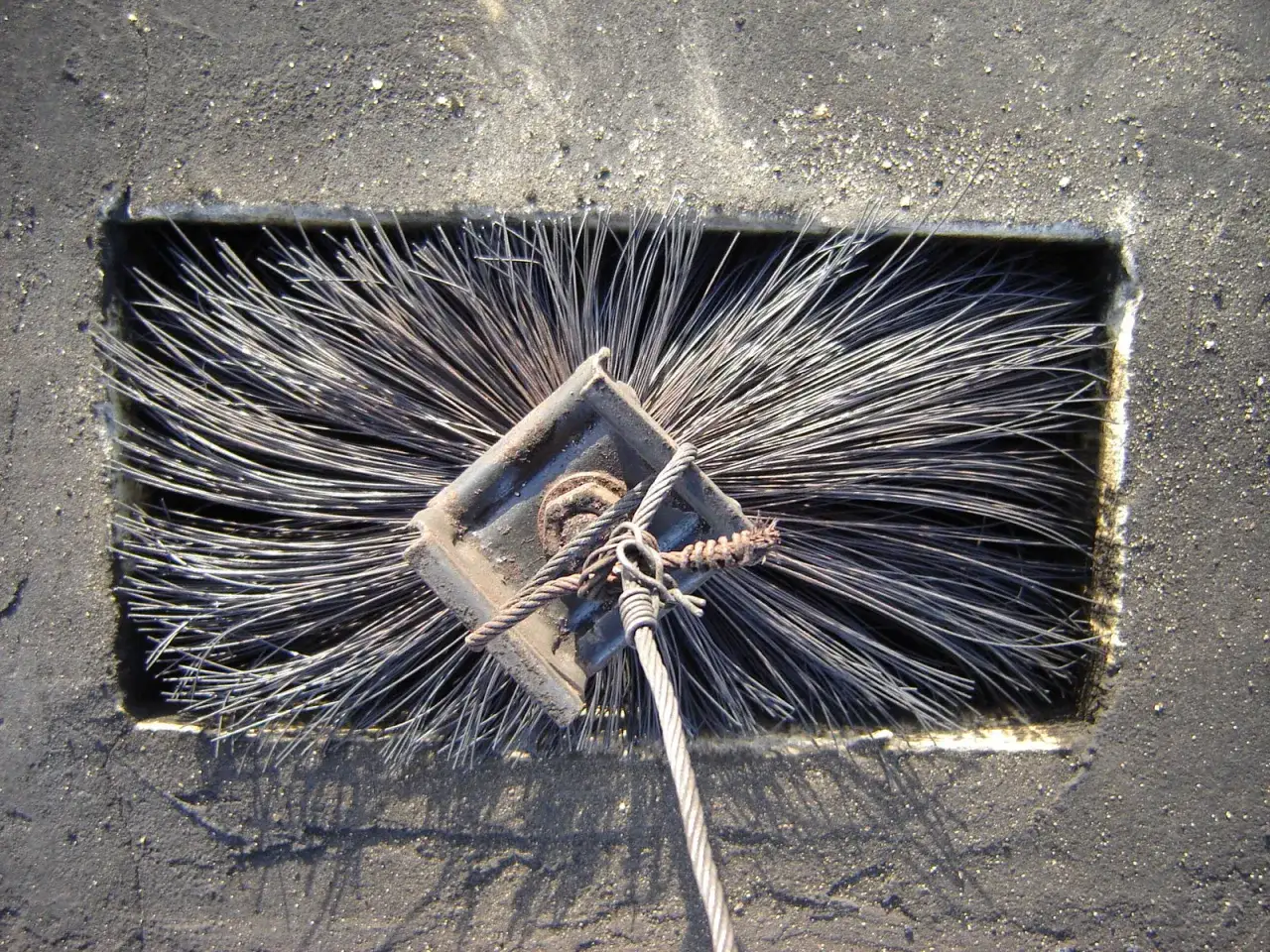 Szczotka do czyszczenia komina, gotowa do użycia. Widać jej druciane włosie i metalowy uchwyt.