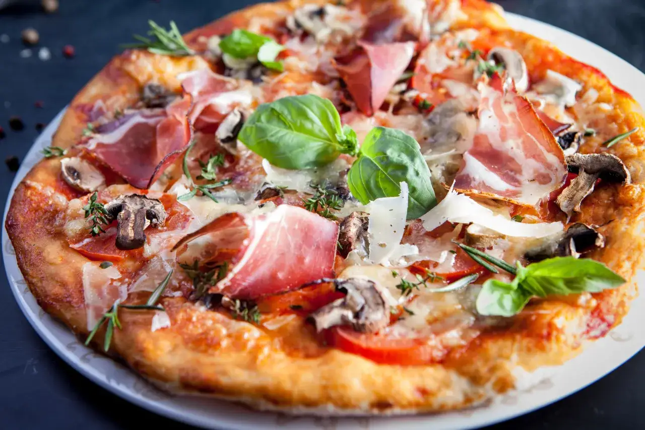 Domowa pizza z prosciutto, pieczarkami, pomidorami i bazylią. Idealna na rodzinny obiad.