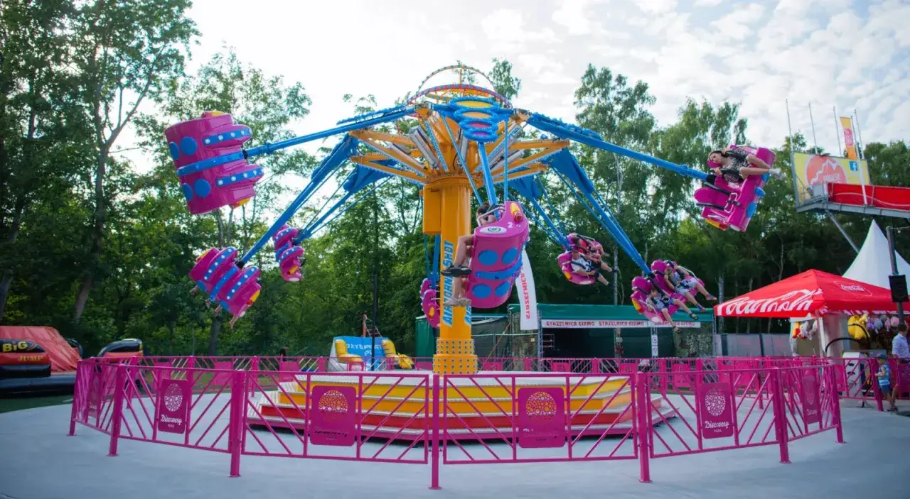 Karuzela w Discovery Park Łeba z kolorowymi gondolami, na których bawią się ludzie.