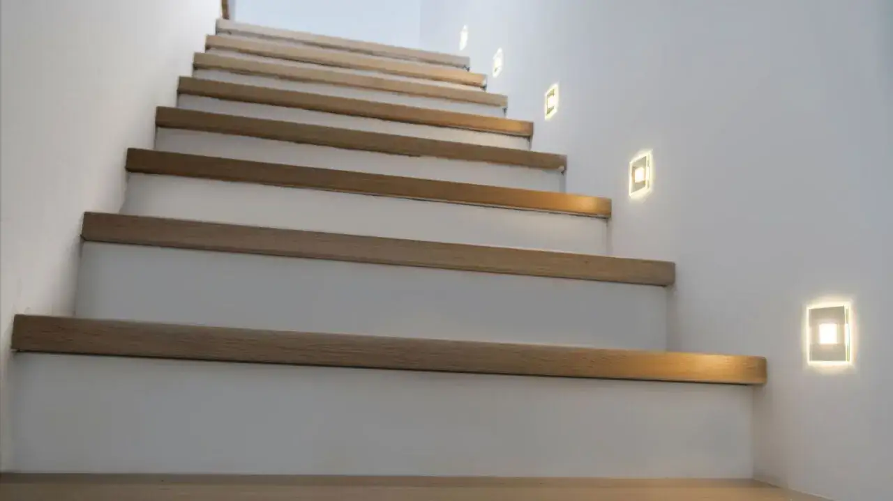 Nowoczesne schody z drewnianymi stopniami i ledy w ścianie przy schodach, tworzące subtelne oświetlenie.