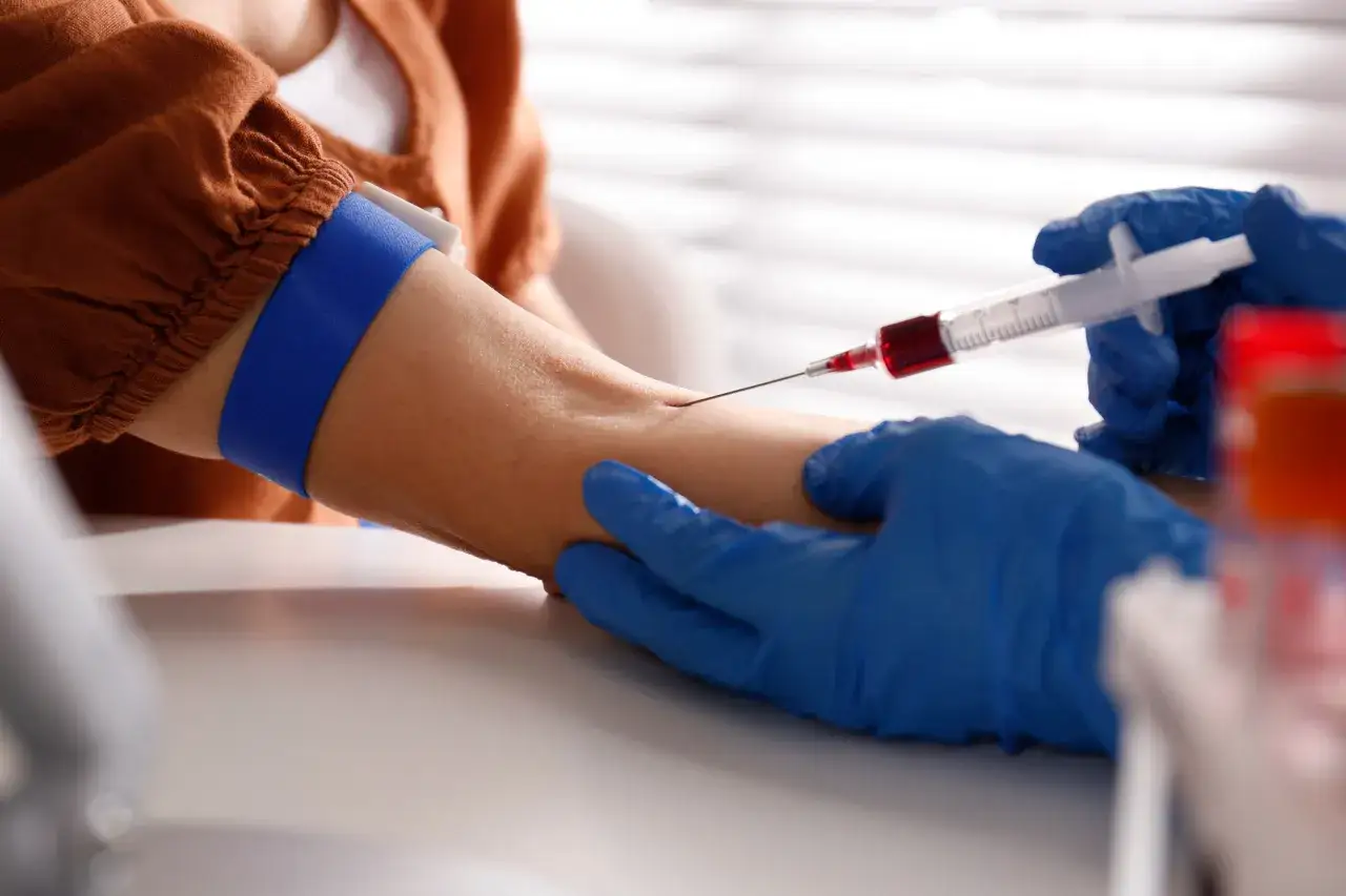 Pobieranie krwi do badań diagnostycznych w laboratorium. Ręka w niebieskiej rękawiczce trzyma strzykawkę z krwią.