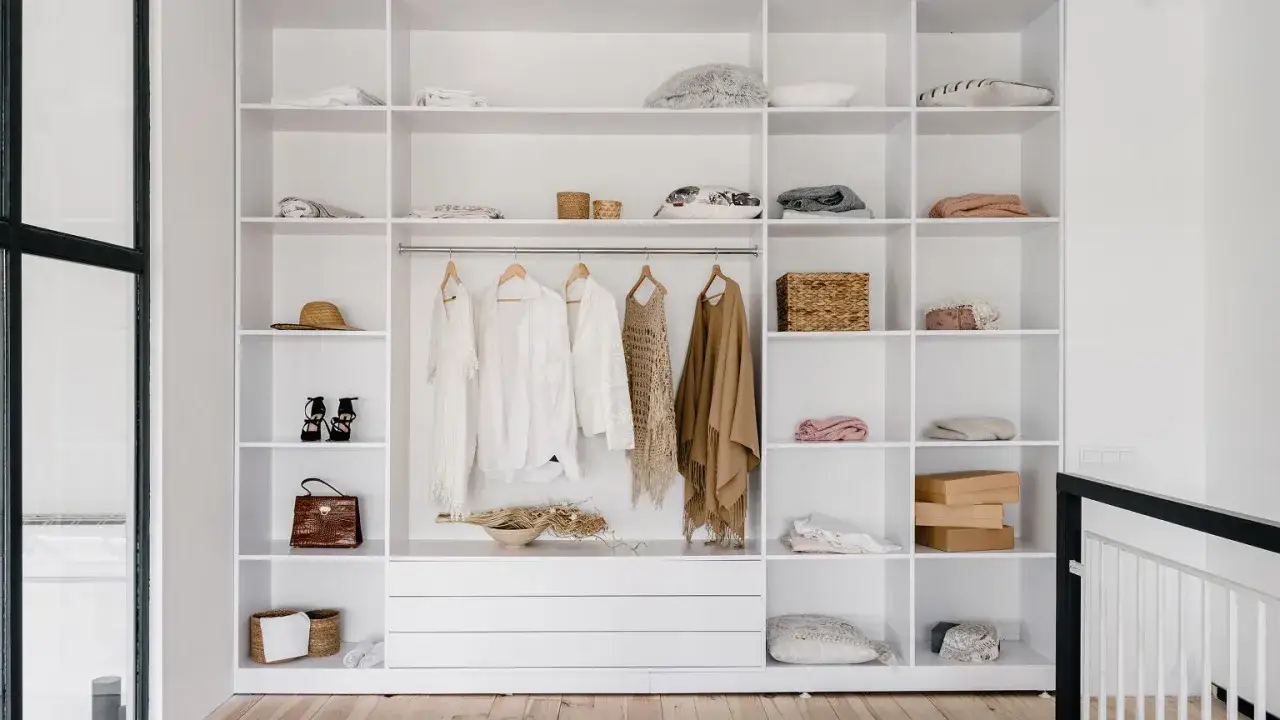 Inspiracja, jak zrobić szafę z drzwiami przesuwnymi: białe, otwarte półki z ubraniami, akcesoriami i dekoracjami.