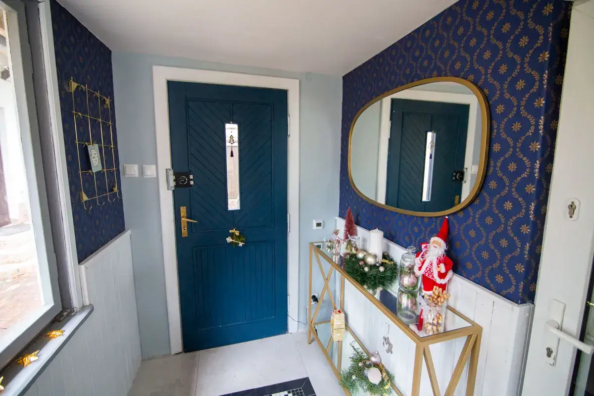 Wnętrze z granatową tapetą na boazerii, ozdobione świątecznymi dekoracjami i niebieskimi drzwiami.