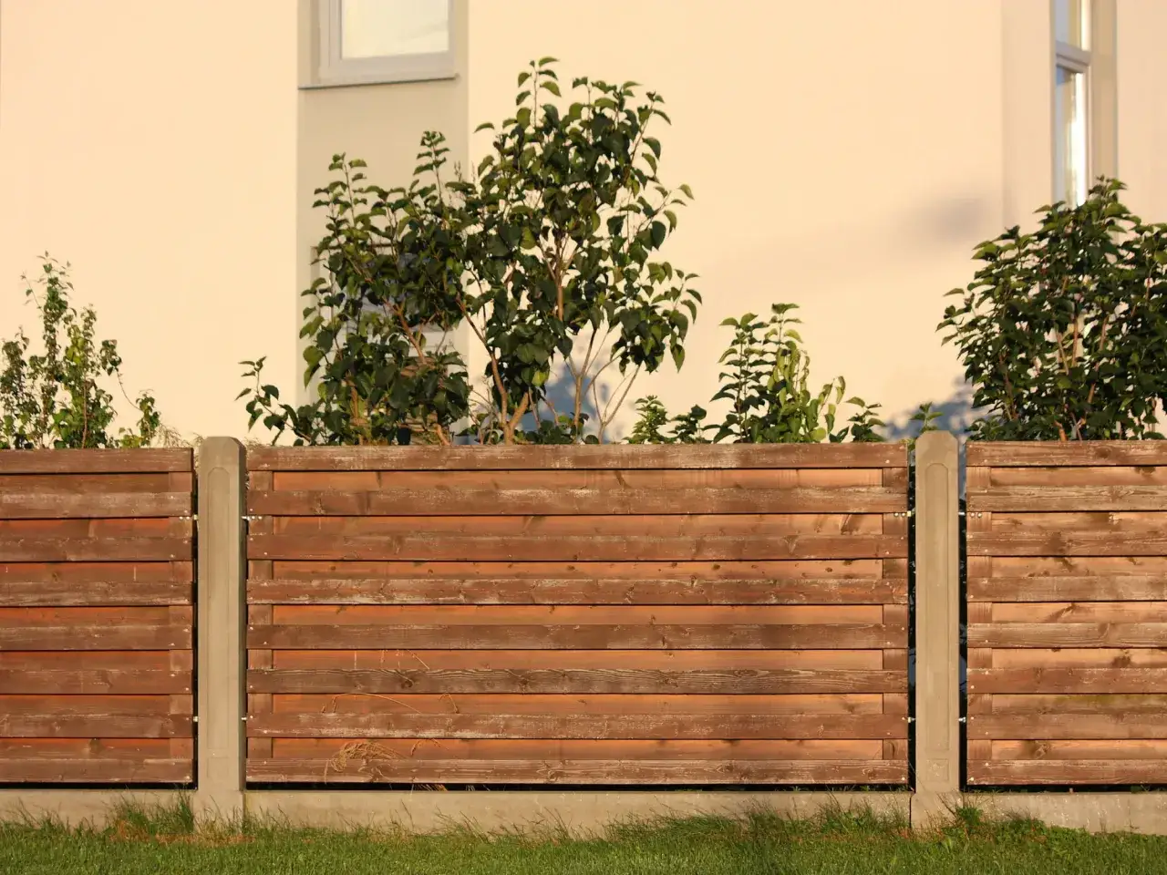 Solidne, drewniane ogrodzenie na taras z betonowymi słupkami, otoczone zielenią.