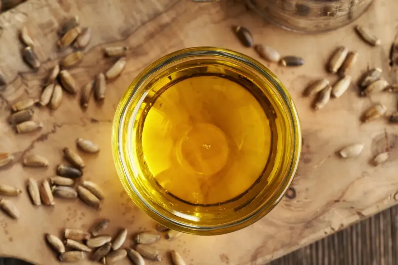 Złocisty olej z ostropestu w szklanej miseczce, otoczony nasionami. Odkryj jego dobroczynne olej z ostropestu na twarz efekty.