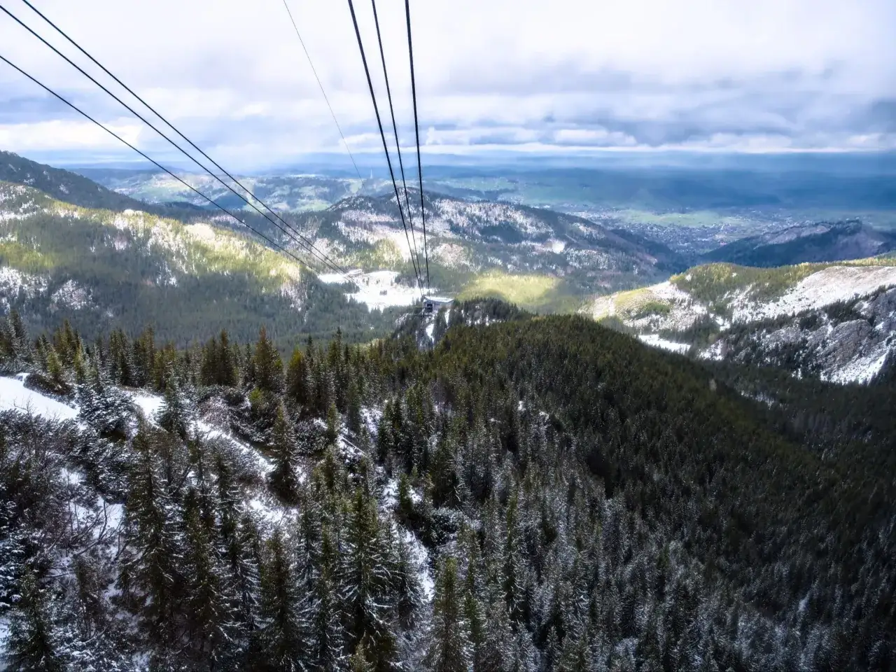 Widok z kolejki na Kasprowy Wierch. Śnieg na drzewach i zboczach g&oacute;r, chmury na niebie.