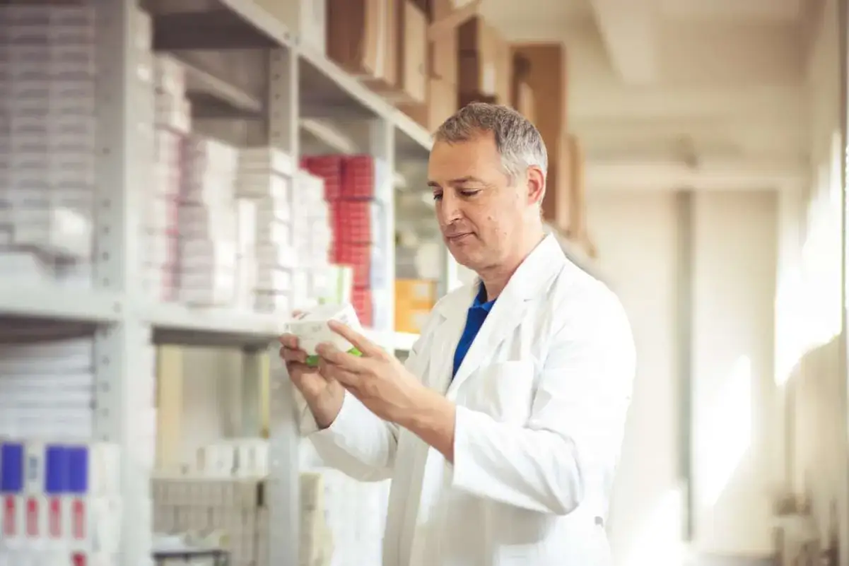 Farmaceuta w białym fartuchu analizuje opakowanie leku. Zastanawia się, ile zarabia technik farmacji, pracując w aptece pełnej leków.