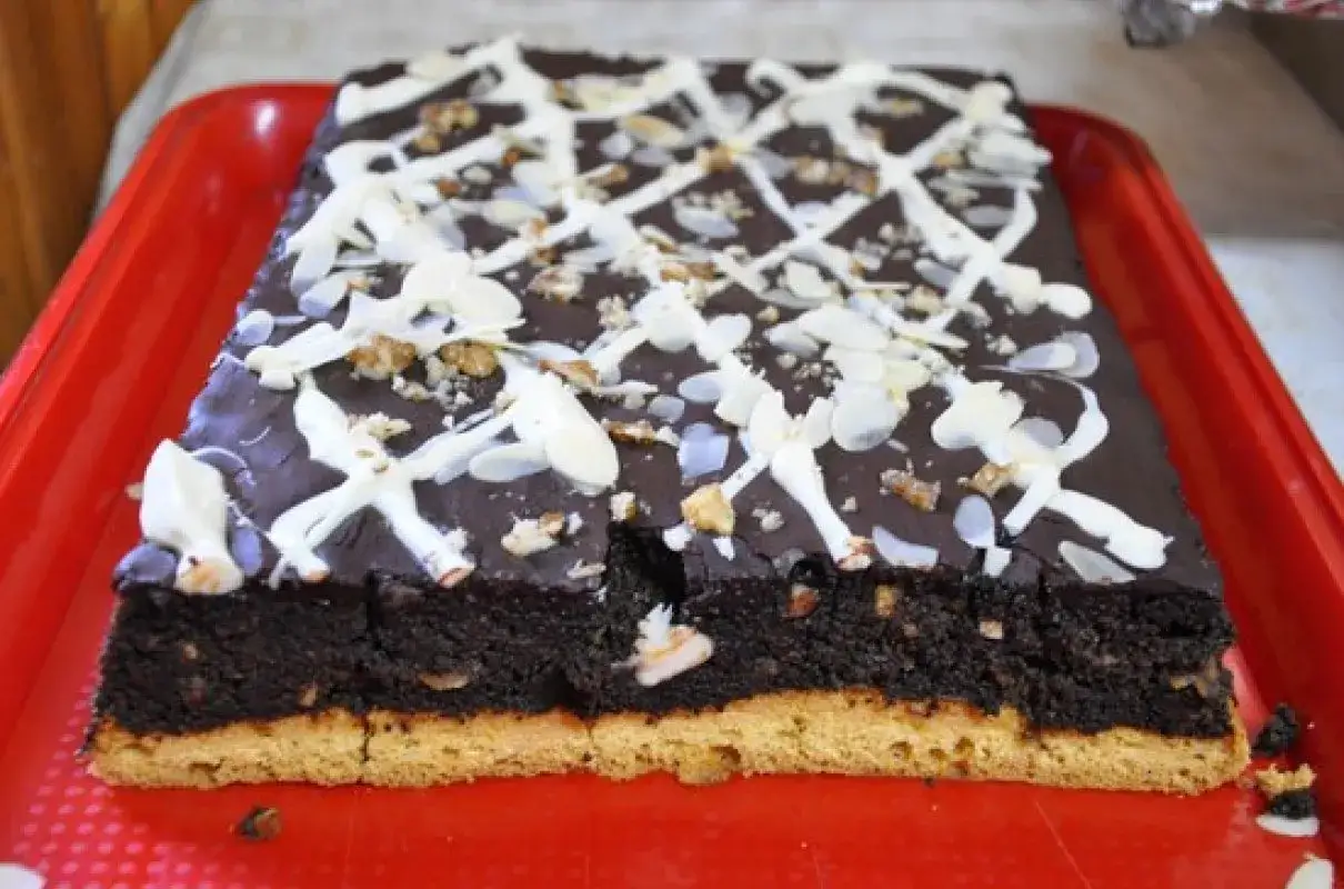 Wilgotny makowiec z gotowej masy makowej, polany czekoladą i posypany płatkami migdał&oacute;w i orzechami.