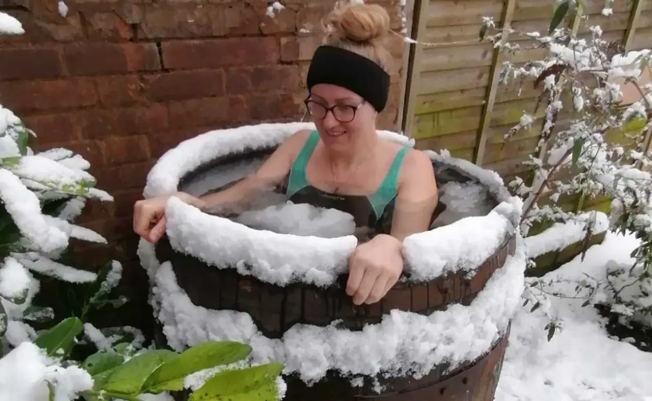 Kobieta w kąpieli lodowej, otoczona śniegiem, praktykuje oddychanie metodą Wima Hofa.