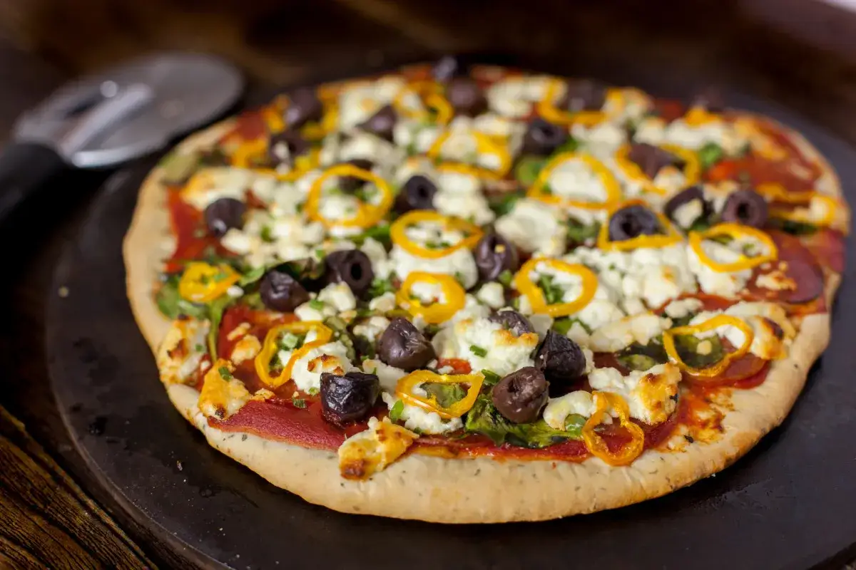 Pyszna pizza na cienkim cieście z fetą, oliwkami, papryką i rukolą. Idealna na szybki obiad.