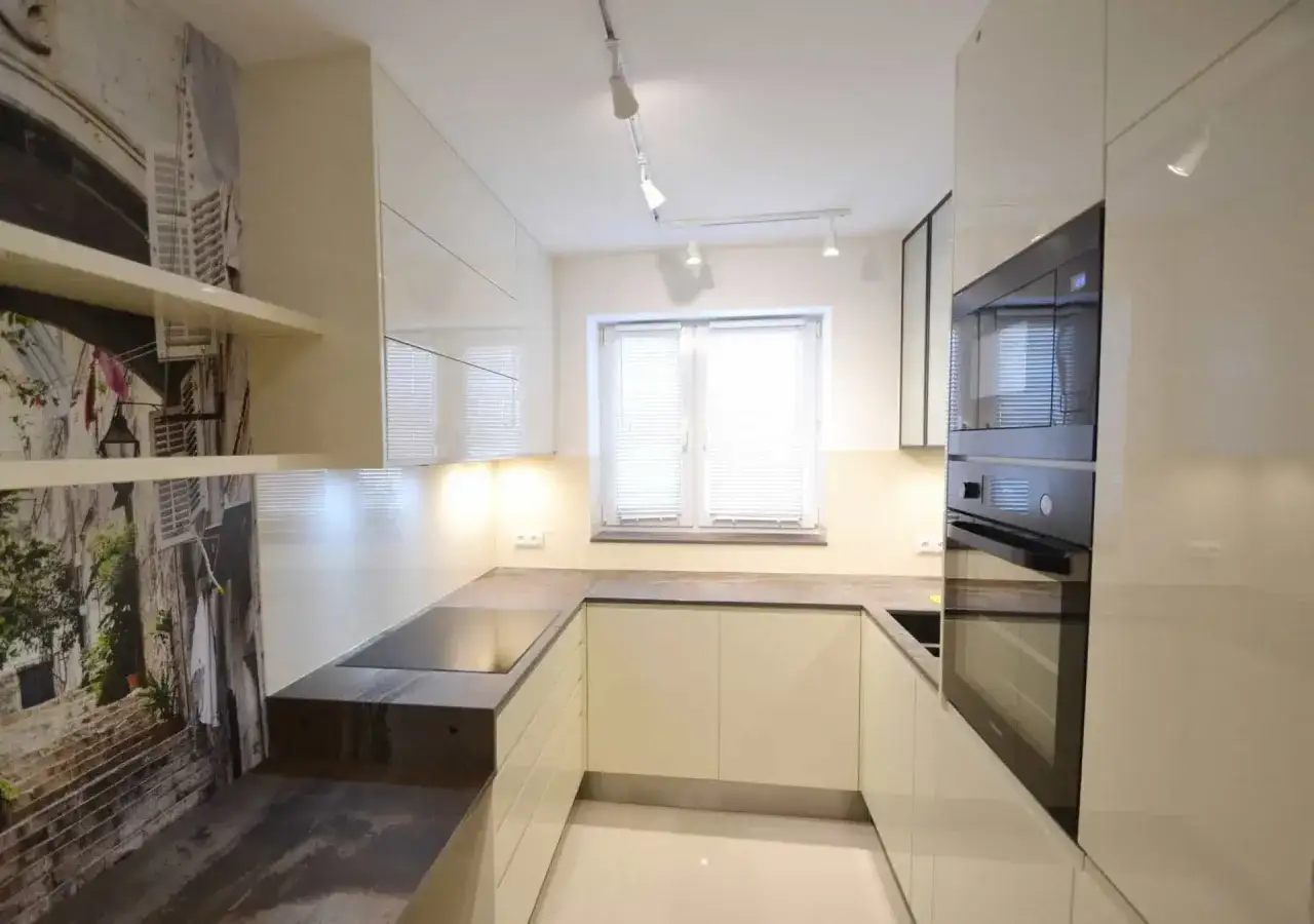 Nowoczesna kuchnia z tapetą imitującą uliczkę. Ciepłe oświetlenie cokołu w kuchni podkreśla zabudowę.