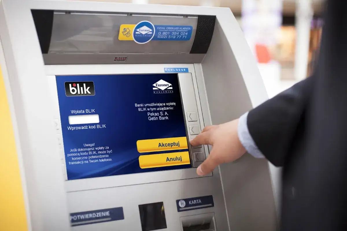 Dłoń klienta wciska przycisk na bankomacie Euronet, kt&oacute;ry umożliwia wpłatę BLIK. Nest Bank oferuje darmowe bankomaty.