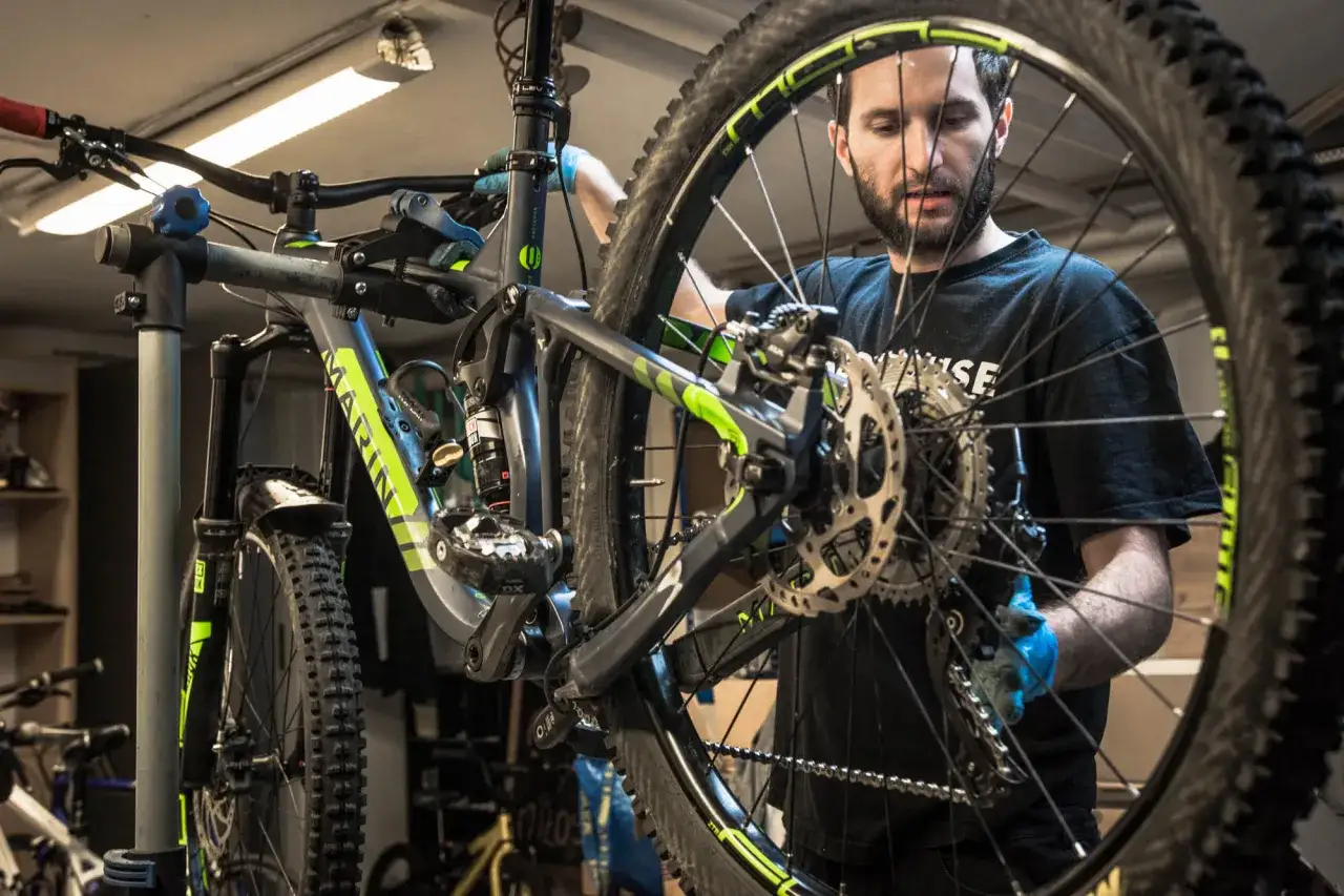 Mężczyzna w niebieskich rękawiczkach pracuje nad składaniem roweru górskiego.