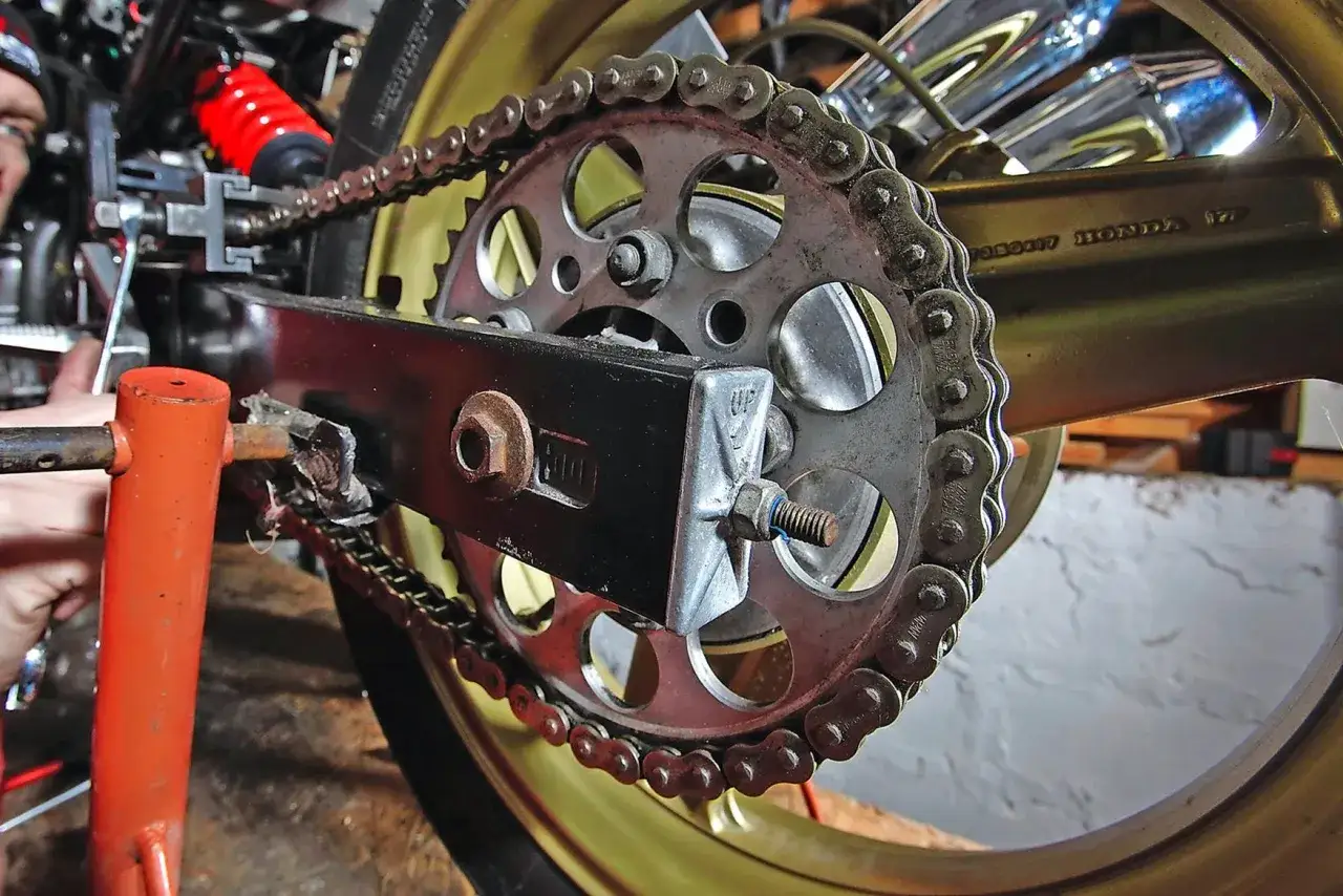 Narzędzie do rozkuwania łańcucha motocyklowego przy zębatce. Widoczny element mocowania, śruba i łańcuch.