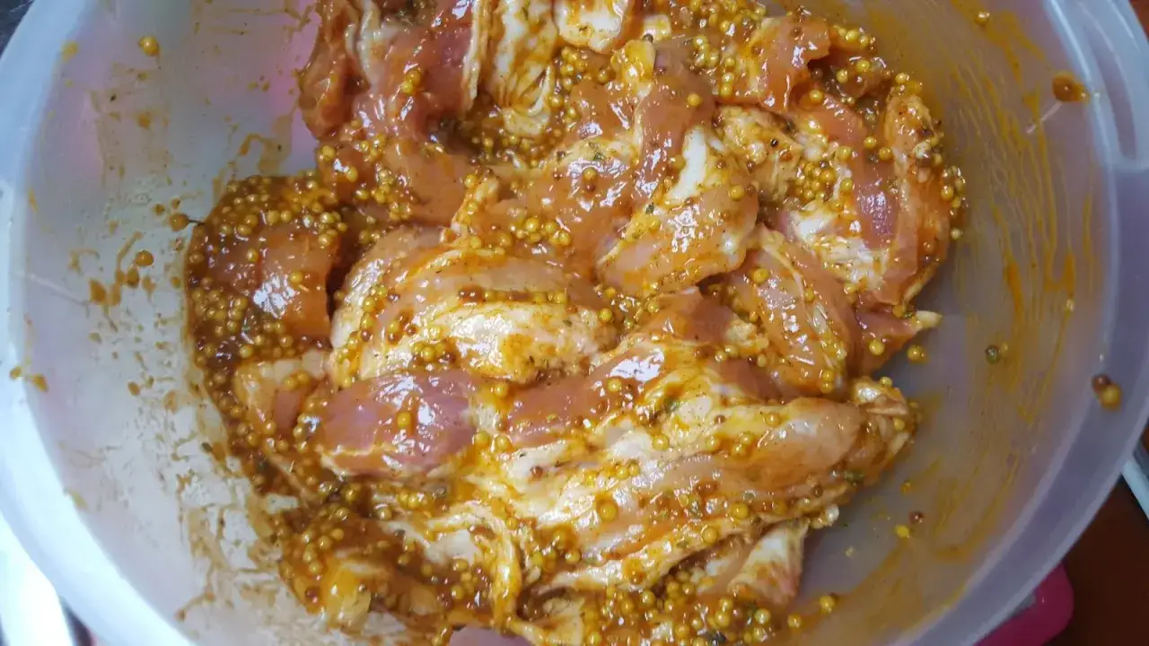 Mięso w misce, gotowe do grillowania, zanurzone w aromatycznej marynacie musztardowo miodowej z całymi ziarnami gorczycy.