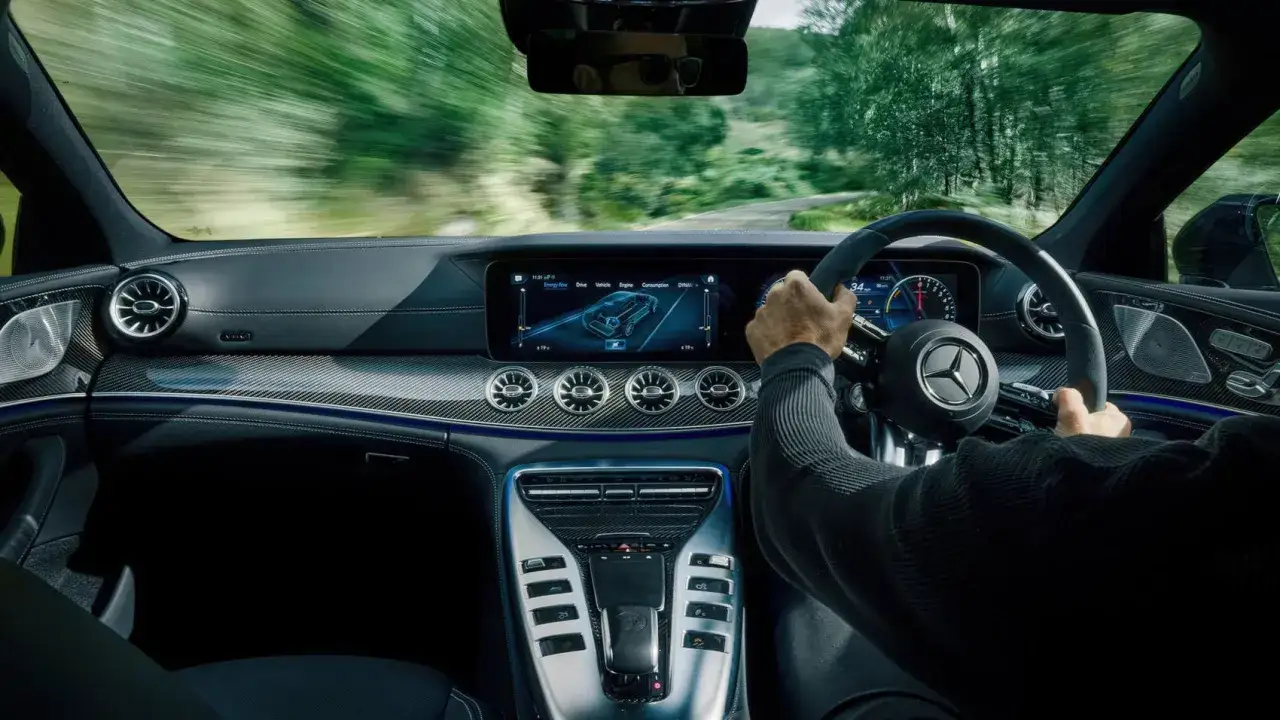 Wnętrze Mercedes-AMG GT 63 S z widokiem na drogę. Kierowca trzyma kierownicę, a na ekranie widnieje schemat samochodu.