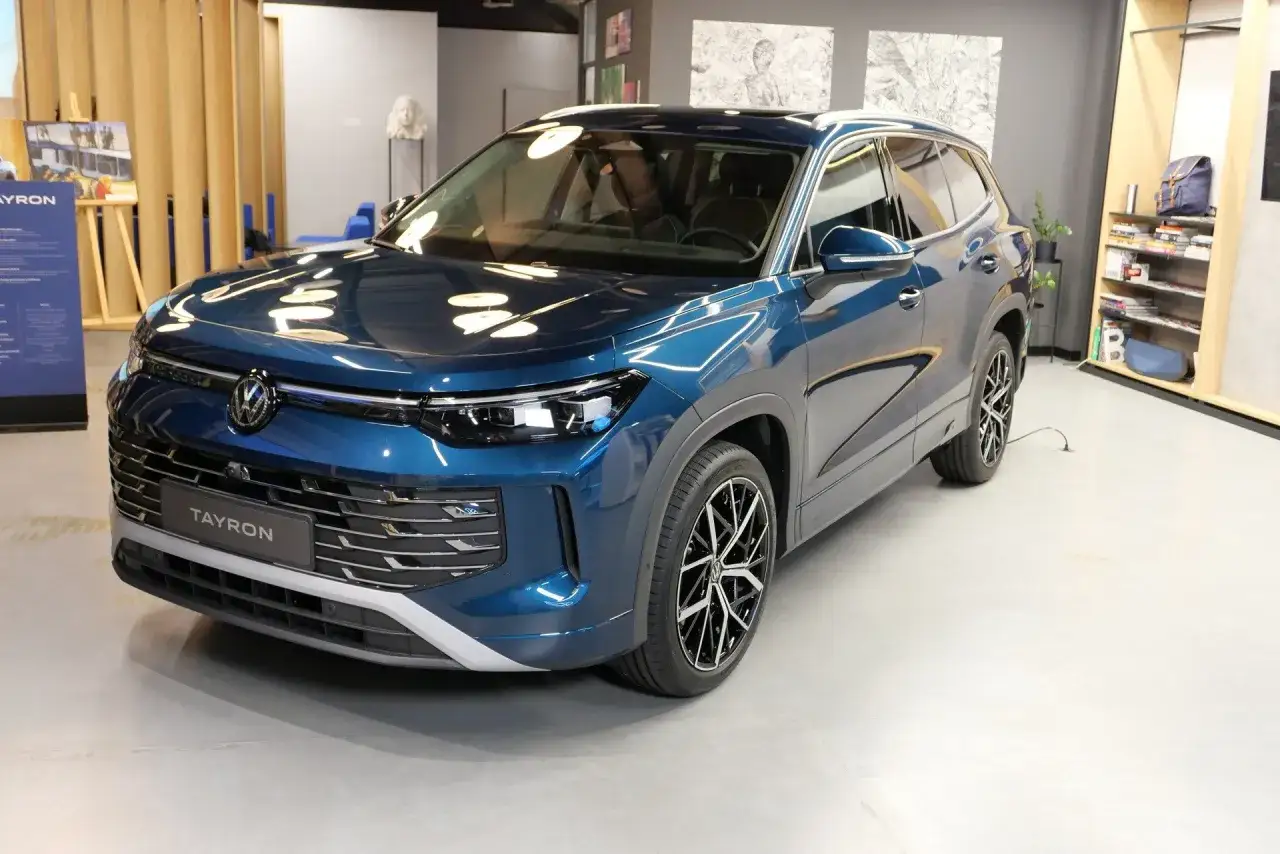 Błękitny Volkswagen Tayron, nowy SUV z charakterystycznym grillem i nowoczesnymi światłami, prezentuje się elegancko w salonie.