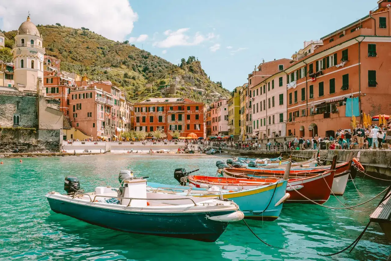 Kolorowe łodzie kołyszą się na turkusowej wodzie w malowniczej zatoce Cinque Terre, z widokiem na pastelowe domy i zielone wzgórza.