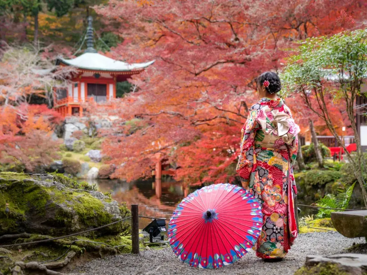 Kobieta w kimonie z parasolką podziwia jesienne liście i pagodę. Idealny czas, kiedy najlepiej lecieć do Japonii, by zobaczyć takie widoki.