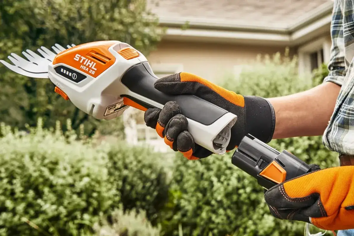 Ręka w rękawicy zakłada baterię do nożyc akumulatorowych do trawy Stihl HSA 26, gotowa do przycinania.