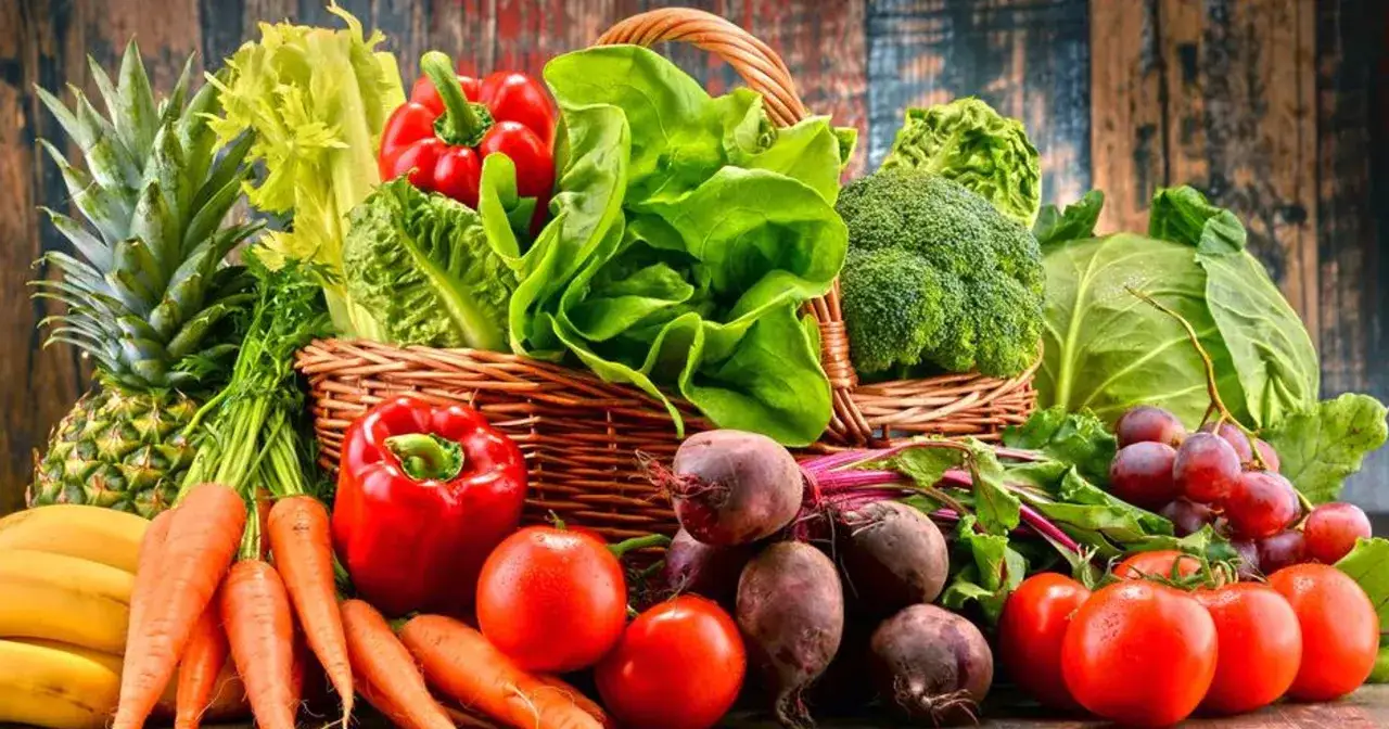 Koszyk pełen świeżych warzyw i owoców, idealnych na dietę owocowo warzywną: ananas, banany, marchew, papryka, pomidory, buraki, sałata, brokuły, kapusta, winogrona.