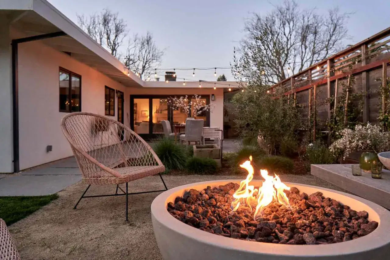 Wieczorne podwórko z paleniskiem, rattanowym fotelem i girlandą żarówek. Idealna lampa do oświetlenia podwórka to taka, która stworzy przytulną atmosferę.