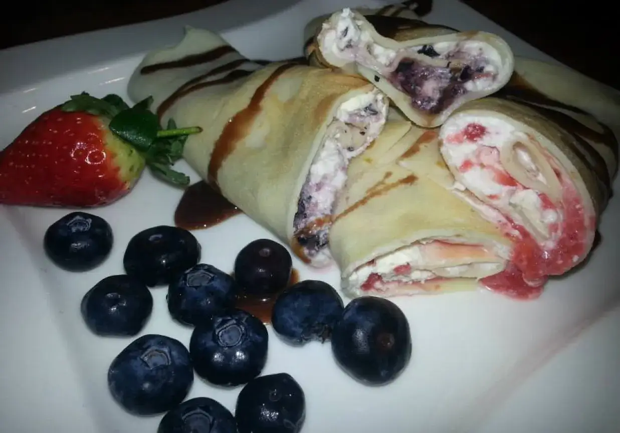 Pyszne naleśniki z serkiem mascarpone, jagodami i truskawkami, polane czekoladą.