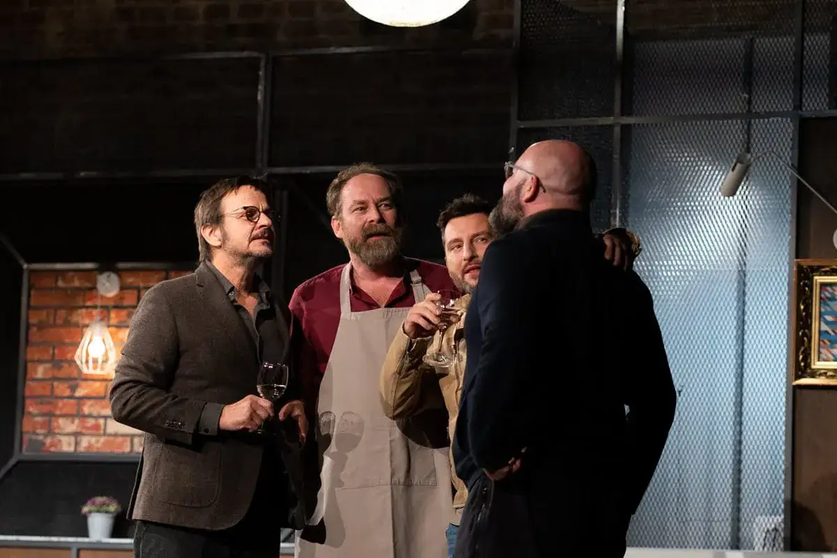 Czterech mężczyzn rozmawia przy kieliszkach wina na scenie. Spektakl 