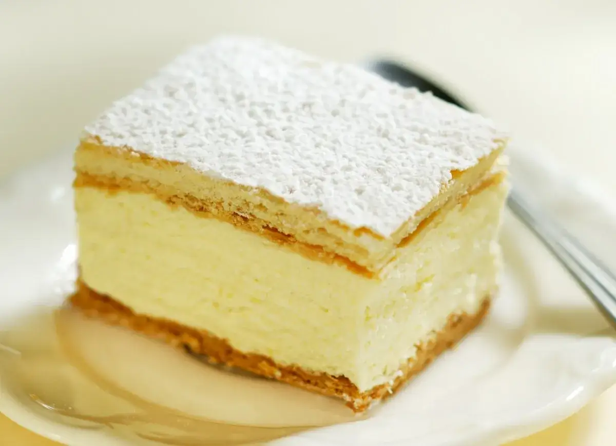 Krem custard i krem budyniowy w cieście francuskim, posypane cukrem pudrem. Pyszny deser na talerzyku.