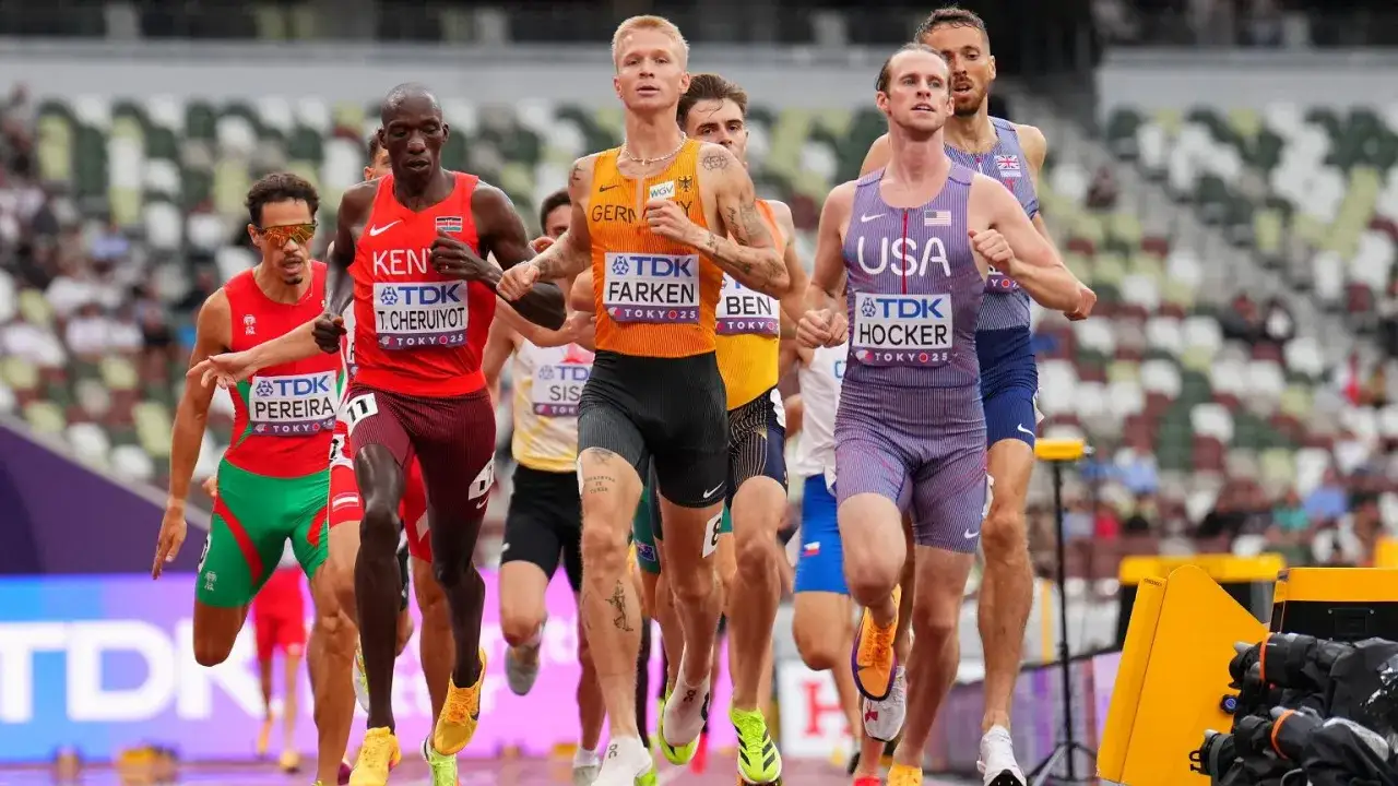 Biegacze na bieżni, w tym zawodnicy z Kenii, Niemiec i USA. Sędzia na bieżni obserwuje zmagania sportowców.