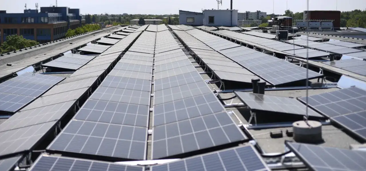 Rzędy paneli fotowoltaicznych na dachu bloku mieszkalnego, zbierające energię słoneczną.