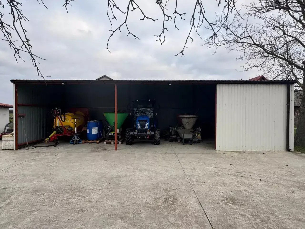 Dobudowa wiaty do budynku gospodarczego chroni sprzęt rolniczy: opryskiwacz, traktor, rozsiewacz.