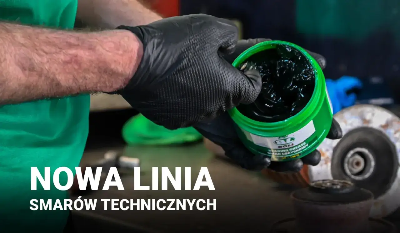 Ręce w czarnych rękawiczkach trzymają zielony pojemnik z ciemnym, gęstym smarem stałym. Nowa linia smar&oacute;w technicznych.