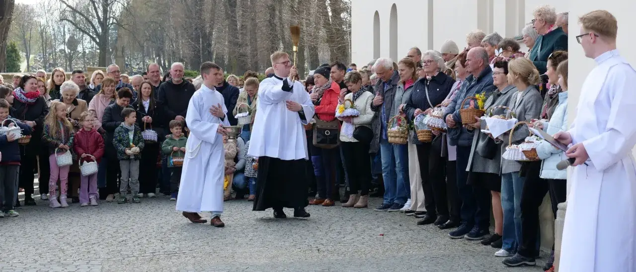 Uroczystość przed bazyliką w Mikołowie. Ludzie z koszykami wielkanocnymi, księża w strojach.