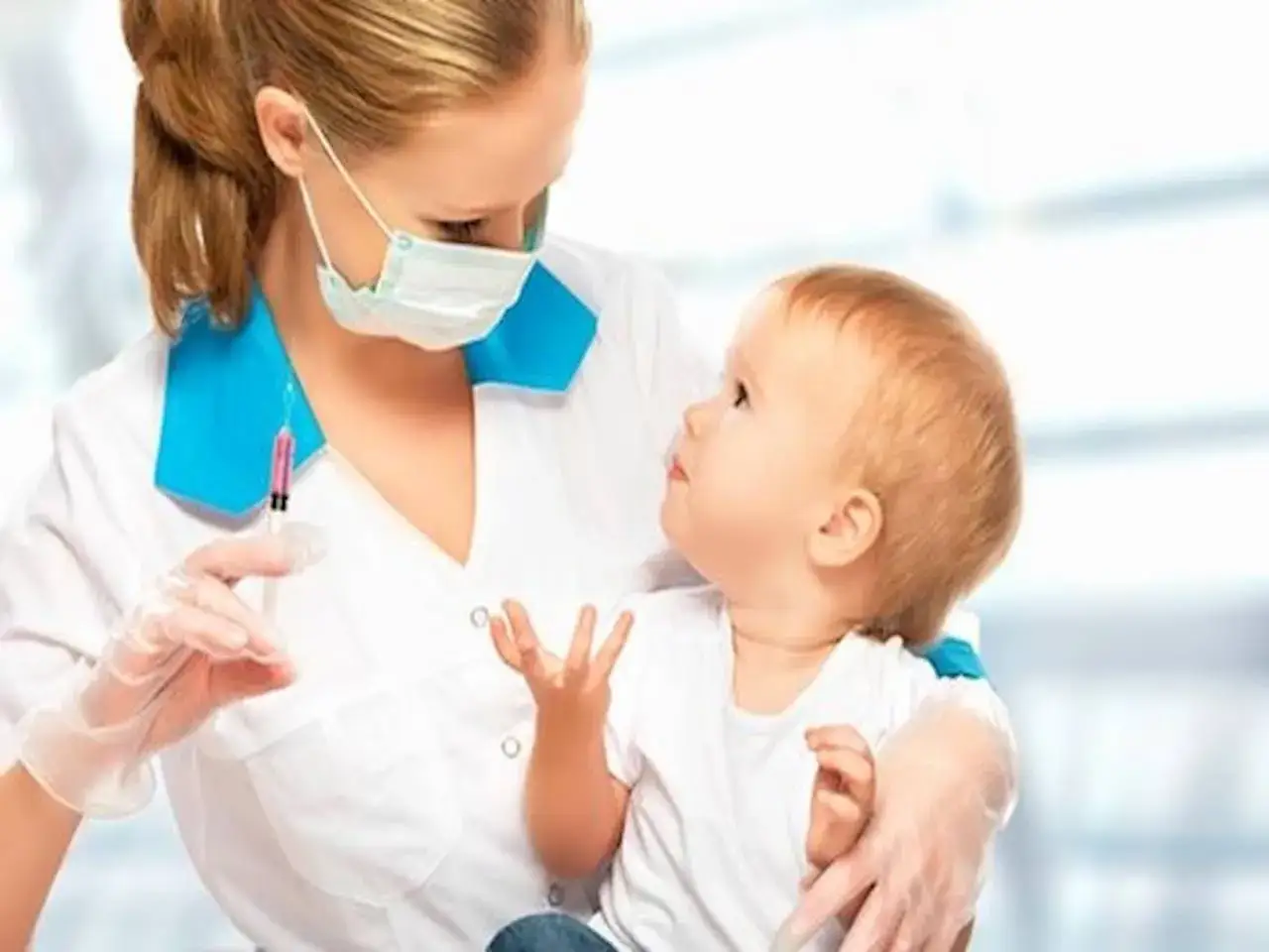 Pielęgniarka w maseczce i rękawiczkach trzyma strzykawkę z r&oacute;żowym płynem, gotowa do podania szczepionki 6w1 małemu dziecku.