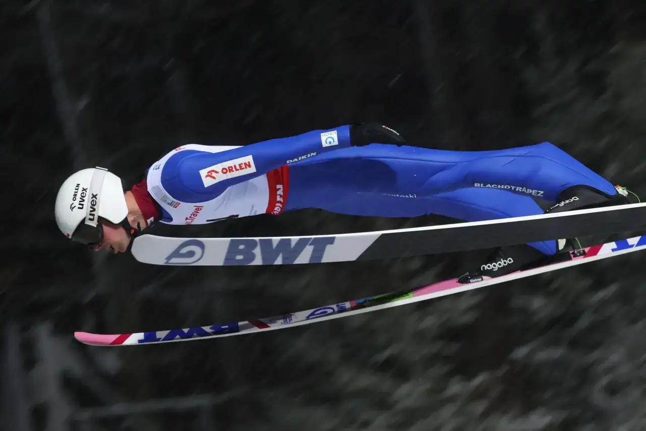 Skoczek narciarski w locie podczas Pucharu Świata w Wiśle, w niebieskim kombinezonie z logo Orlen.