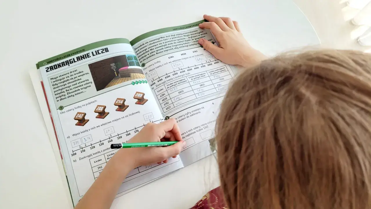 Dziecko rozwiązuje zadania z matematyki z elementami Minecrafta, ćwicząc zaokrąglanie liczb.