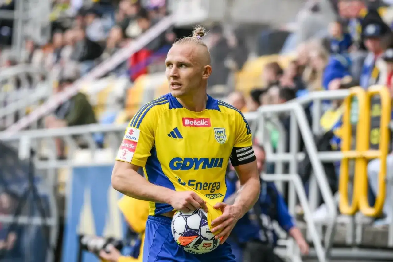 Piłkarz Arki Gdynia z piłką, w żółtej koszulce, walczy o to, kto awansuje do ekstraklasy.