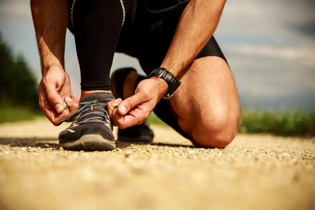 Biegacz na żwirowej ścieżce zawiązuje buty. Czy to początek treningu, czy może drop w bieganiu?