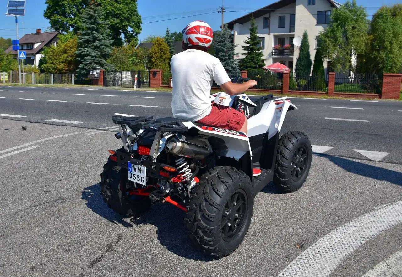 Mężczyzna w kasku jedzie quadem po drodze. Zastanawiasz się, jakie prawo jazdy na quada jest potrzebne?
