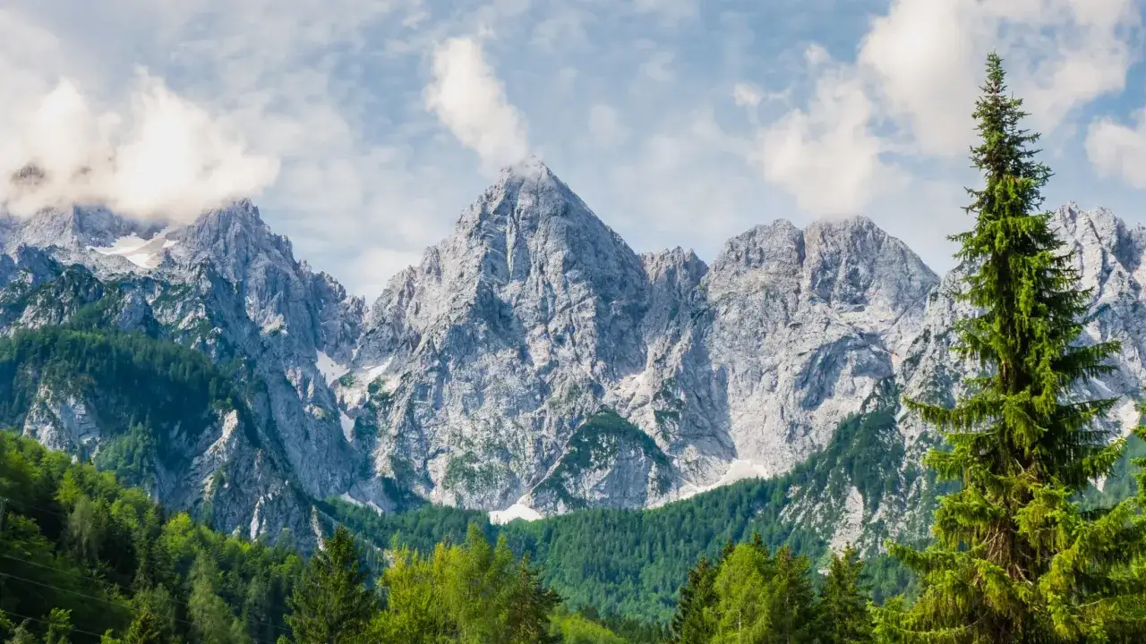 Majestatyczne góry w Słowenii, pokryte śniegiem i zielonymi lasami. Ceny noclegów w tym regionie są bardzo zróżnicowane.