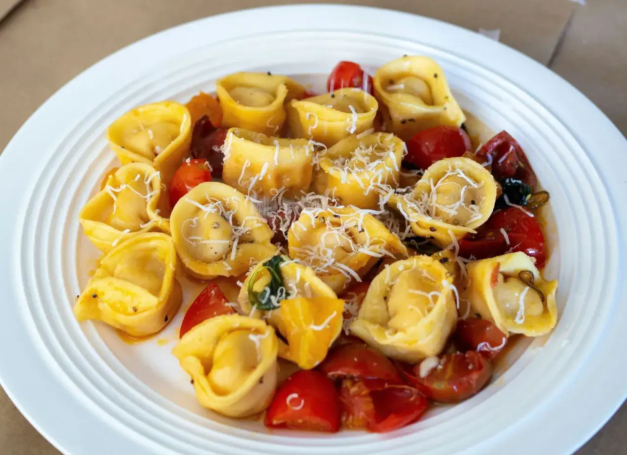 Pyszne tortellini in brodo przepis. Złociste pierożki z pomidorkami i parmezanem na białym talerzu.