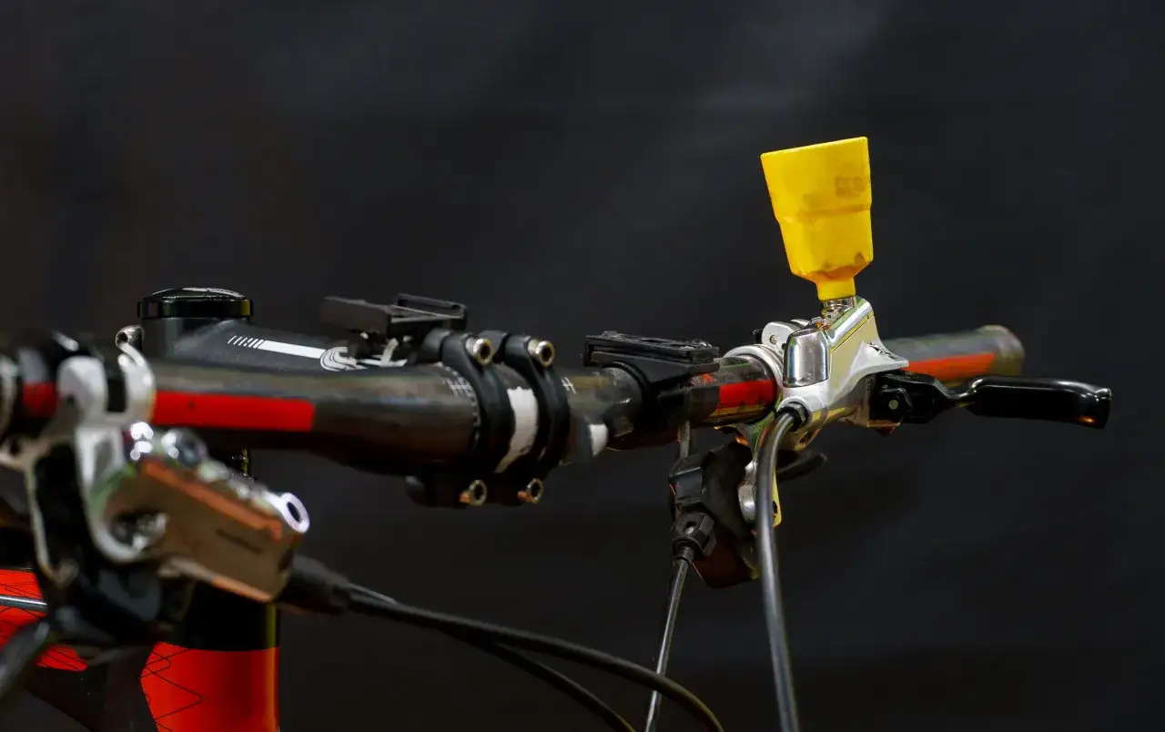 Jak odpowietrzyć hamulce w rowerze bez odpowietrznika? Widoczny żółty lejek na kierownicy roweru, podłączony do hamulca, sugeruje sposób na odpowietrzenie.