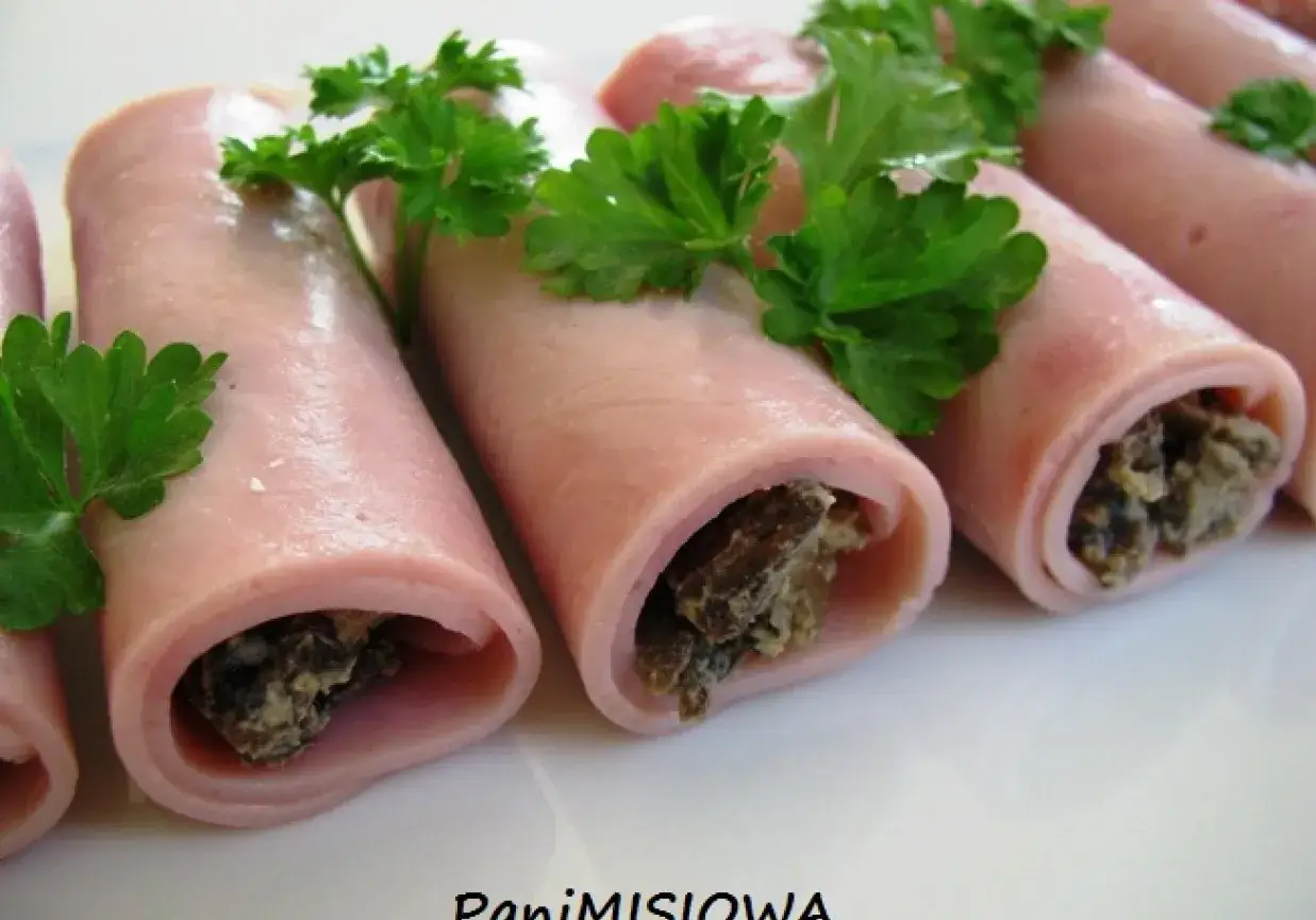 Roladki z szynki konserwowej z farszem grzybowym, udekorowane natką pietruszki. Pyszna przekąska na każdą okazję.