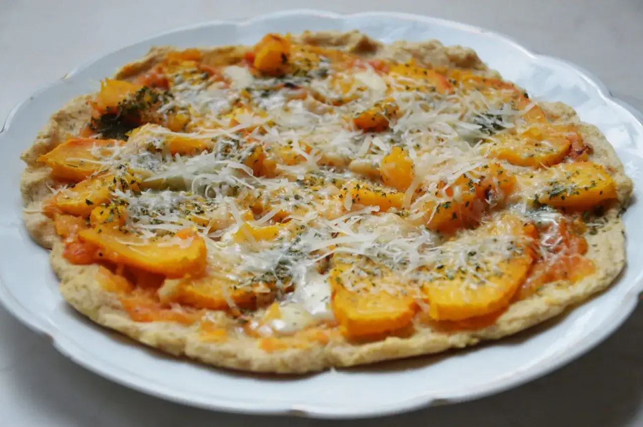 Pizza z dynią i pomidorami, posypana startym parmezanem do pizzy i ziołami.