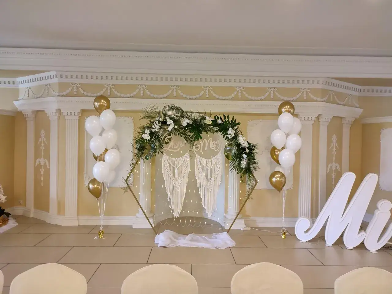 Elegancki łuk do balonów z kwiatami i makramą, ozdobiony białymi i złotymi balonami. Idealna dekoracja na ślub.