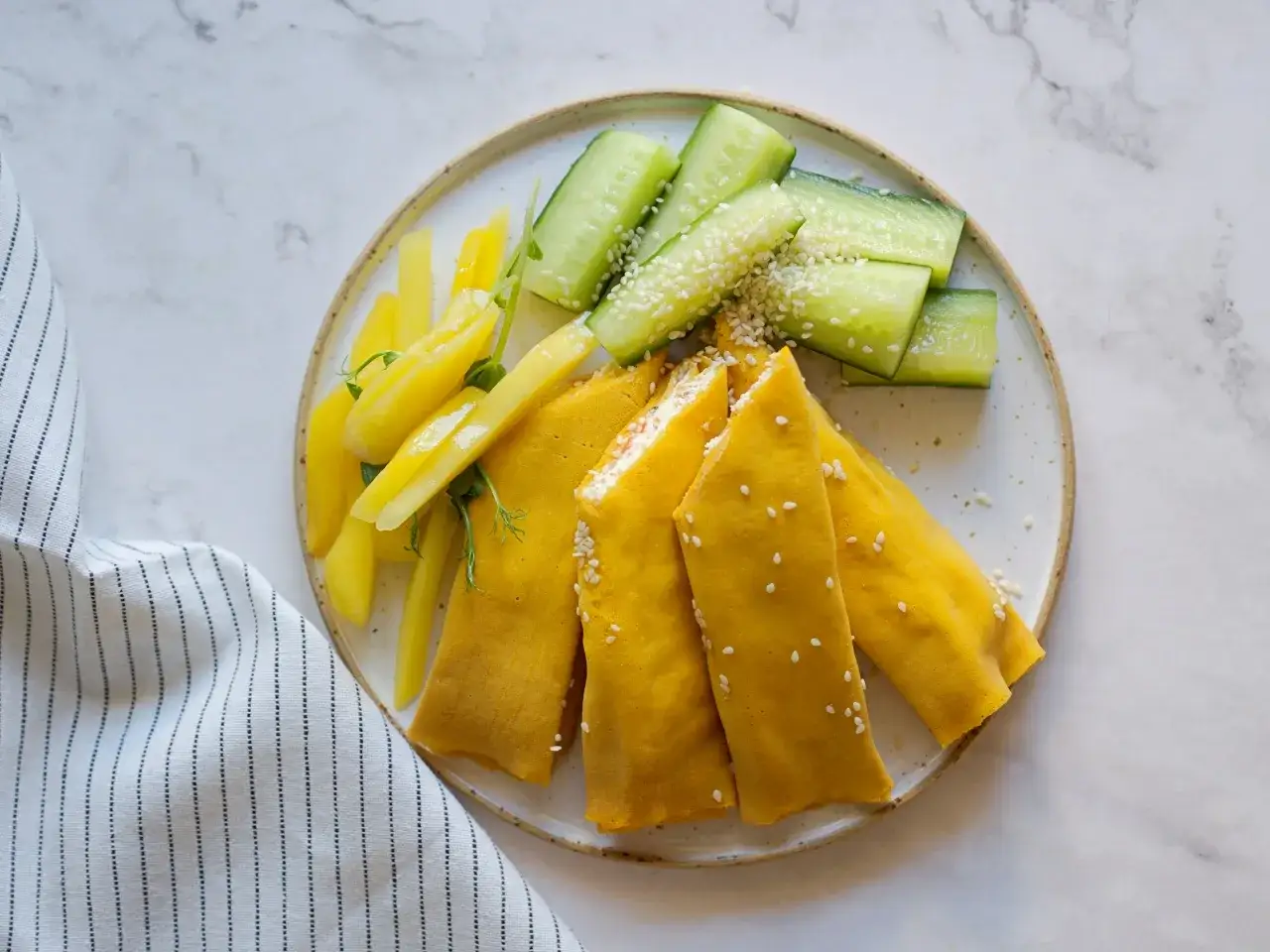 Żółte naleśniki z farszem, ogórek i żółta papryka na talerzu. Czy warto wybrać catering dietetyczny?