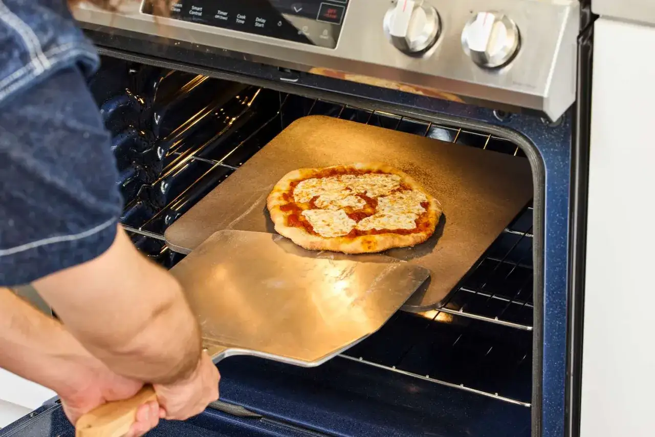 Osoba wkłada pizzę na kamień do pieczenia w piekarniku. Idealny spos&oacute;b, na czym piec pizzę w domu.