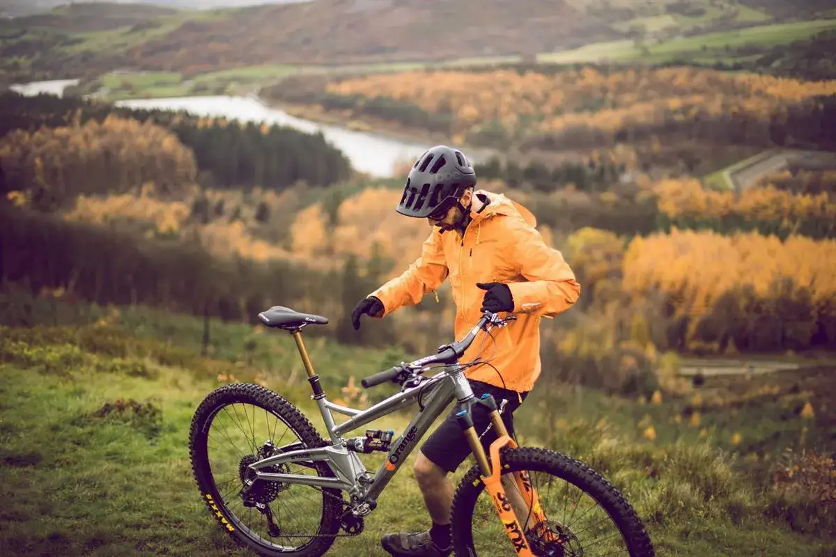 Rowerzysta w pomarańczowej kurtce i kasku przygotowuje się do jazdy. Zanim ruszysz, dowiedz się, jak zmierzyć głowę do kasku, by zapewnić sobie bezpieczeństwo.